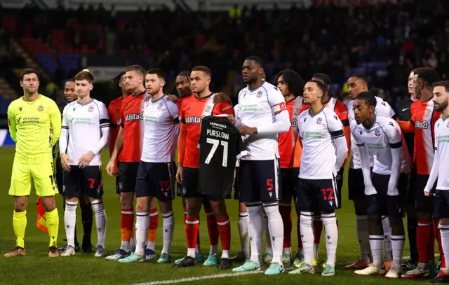 The team captains of Bolton Wanderers and Luton Town hold up a shirt featuring the name of Bolton Wanderers fan Iain Purslow who died on Saturday, ahead of the Emirates FA Cup third round replay match at the Toughsheet Community Stadium, Bolton