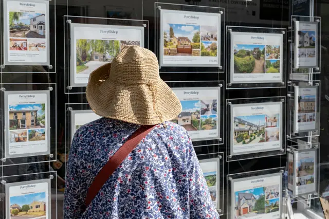 Woman looking at houses for sale in an estate agents window in Cirencester