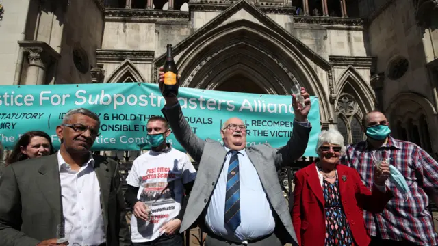 Former post office worker Tom Hedges (centre) holds up a bottle and glass of champagne in celebration outside the Royal Courts of Justice, London, after having his conviction overturned by the Court of Appeal