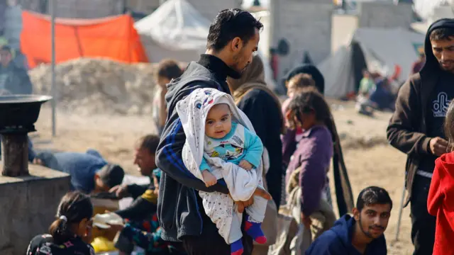 A man holds a baby as displaced Palestinians shelter in a tent camp in Rafah