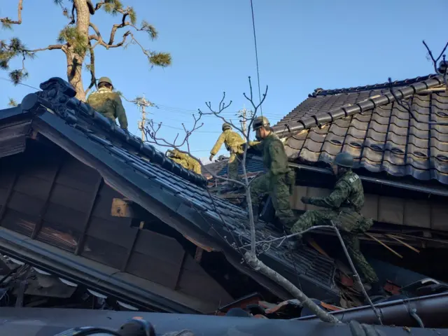 Japanese Self-Defense Force soldiers and firefighters conduct rescue operations at a collapsed house