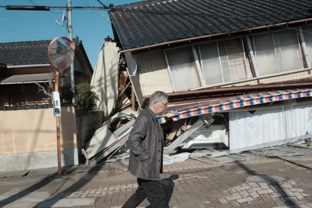 A man walks past a collapsed house in Nanao