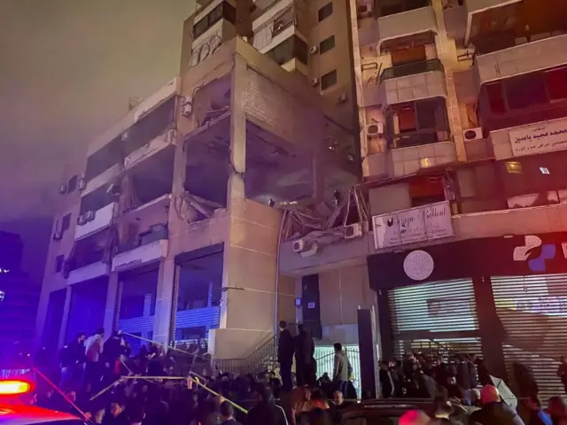 A large group outside a damaged building