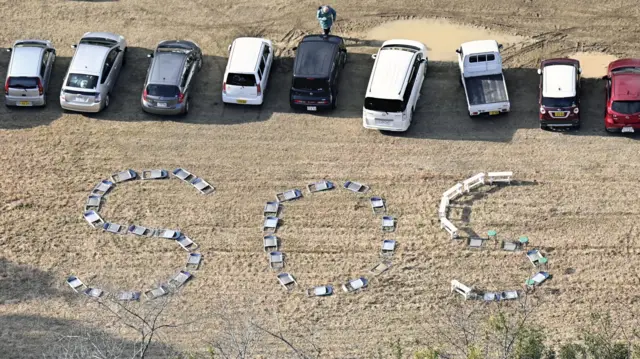 The letters "SOS" are seen written on the ground by using chairs at Kanazawa University