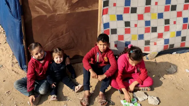 Displaced children sit next to a tent in Rafah, Gaza