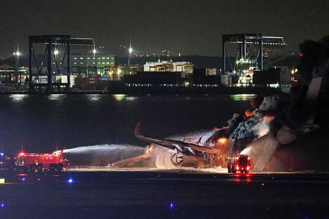 firefighters attempting to extinguish a fire on a Japan Airlines plane on a runway of Tokyo's Haneda Airport