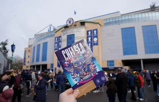 A fan holds up a match programme outside Stamford Bridge.