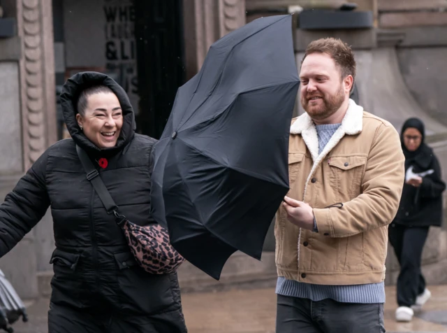 A man struggles with an umbrella in windy conditions in Leeds.