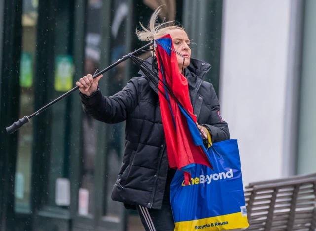 A woman with a broken umbrella in windy conditions in Leeds.