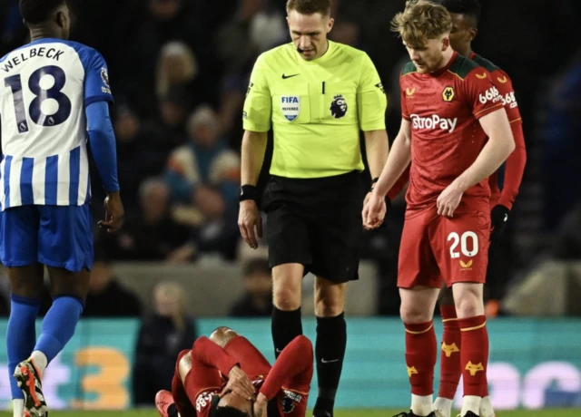 Matheus Cunha reacts after sustaining an injury as Tommy Doyle and referee Craig Pawson look on