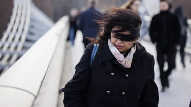 Woman crosses London's Millennium Bridge as the strong winds of Storm Isha cause disruptions across the UK