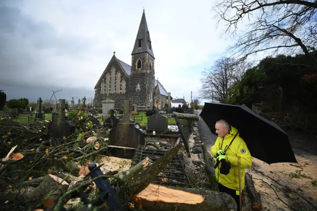 A local resident looks at the damage caused by a fallen tree that fell into the graveyard at St Joseph's Church in Glenavy, Northern Ireland