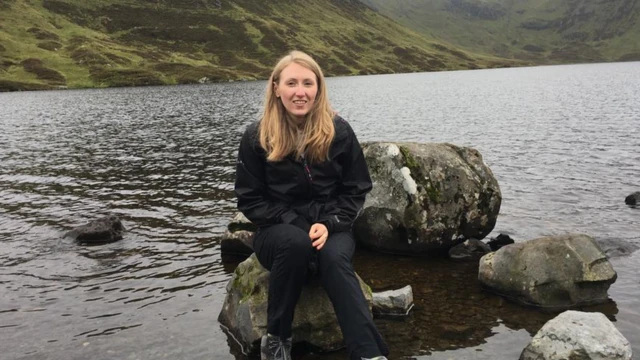 Kerry Hamilton sits on a rock by some water