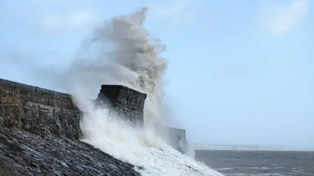 A wave crashes against a sea wall