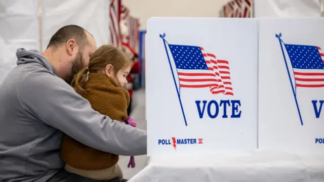 A man casts his ballot with his daughter on his lap inside the polling both