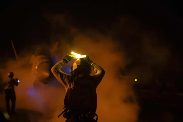 A man holding up lights, conducting flight operations in front of a plane