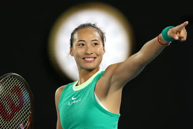 Qinwen Zheng points to the crowd and smiles in celebration wearing a green Nike dress