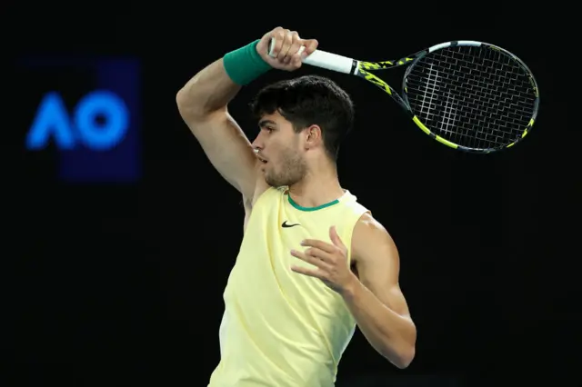 Carlos Alcaraz hits a forehand wearing a light yellow Nike vest