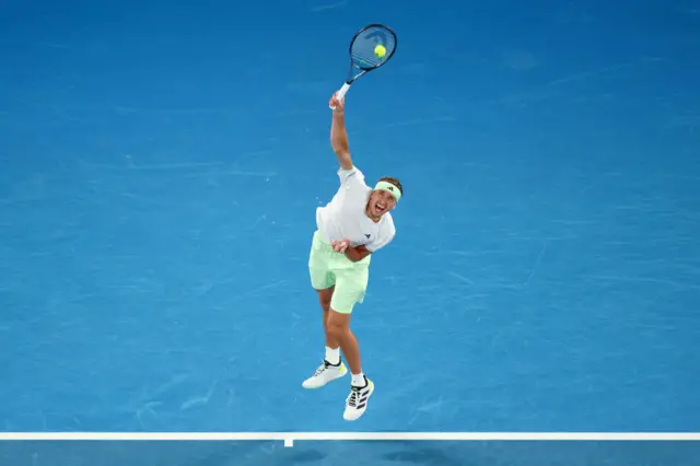 Alexander Zverev serves wearing a white Adidas shirt and cream shorts