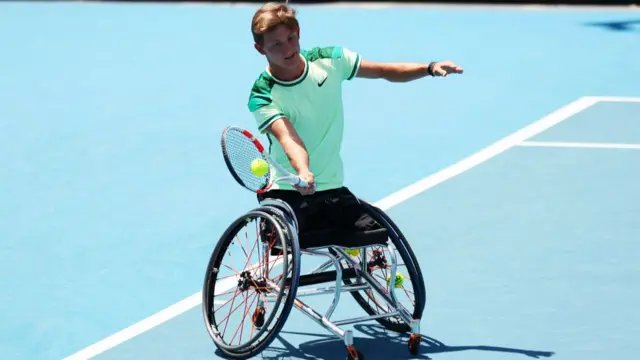 Niels Vink plays a forehand volley wearing a white cream Nike top with green shoulder patterns and a black trim on the sleeves