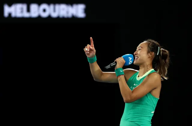 Qinwen Zheng holds the microphone and smiles in her on-court interview