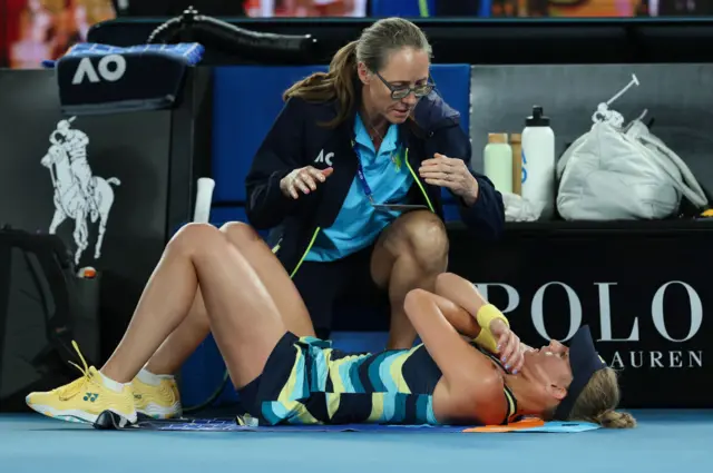 Dayana Yastremska lies flat on her back on a towel on the court and gets treatment from a physio