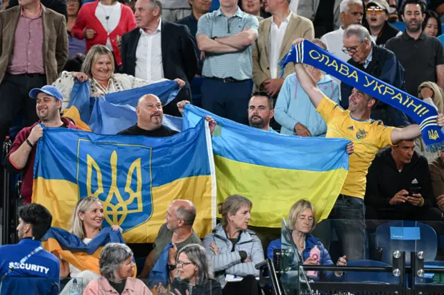 Fans hold Ukrainian flags and scarves