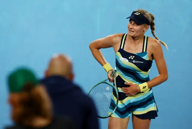 Dayana Yastremska clutches her stomach on the side of the court and looks to her box in above her