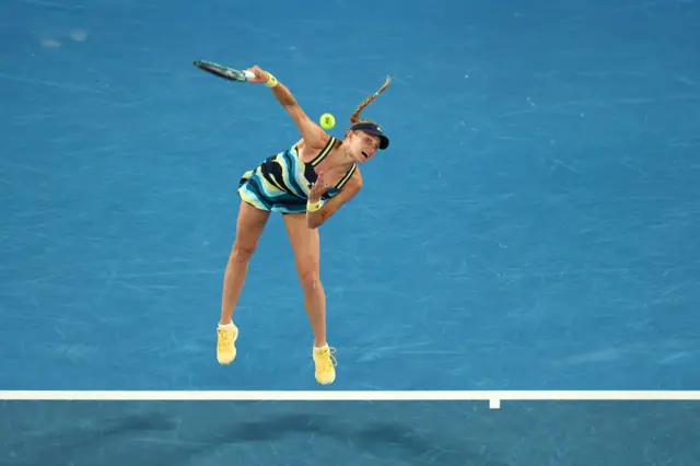 Dayana Yastremska hits a serve wearing a wavy patterned dress with navy blue, yellow and light blue lines