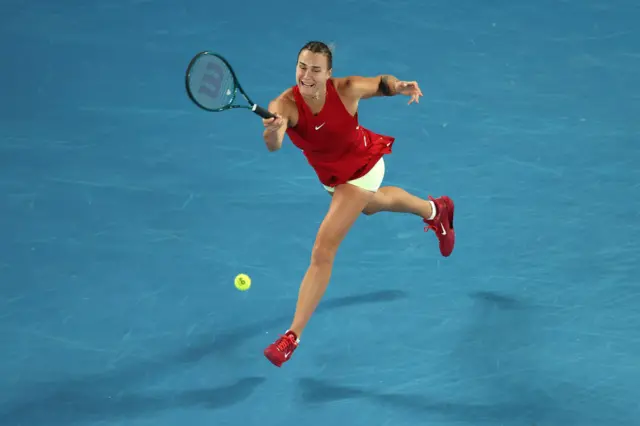 Aryna Sabalenka hits a forehand wearing a red Nike dress