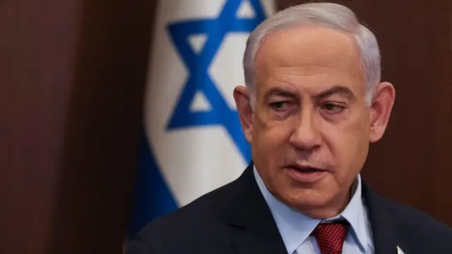 Benjamin Netanyahu stands in front of an Israeli flag