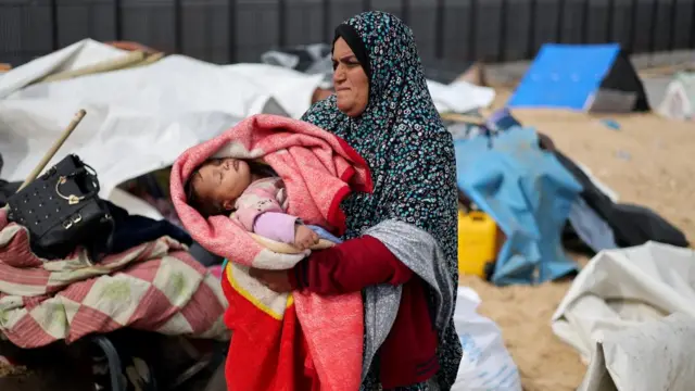 A woman holds a baby as Palestinians fleeing Khan Younis