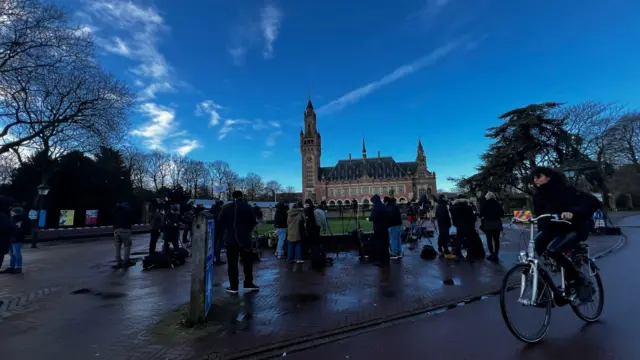 Media crews and woman on bicycle with Peace Palace in background