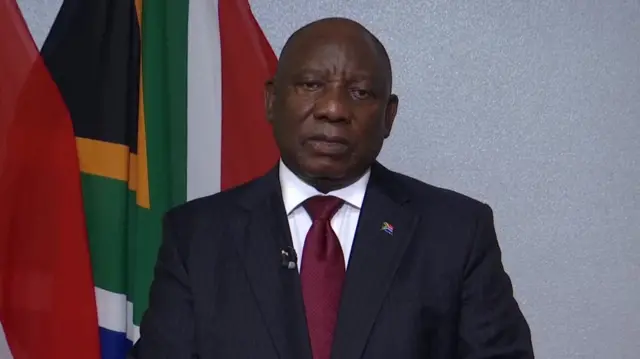 Ramaphosa speaks in front of two hanging south african flags