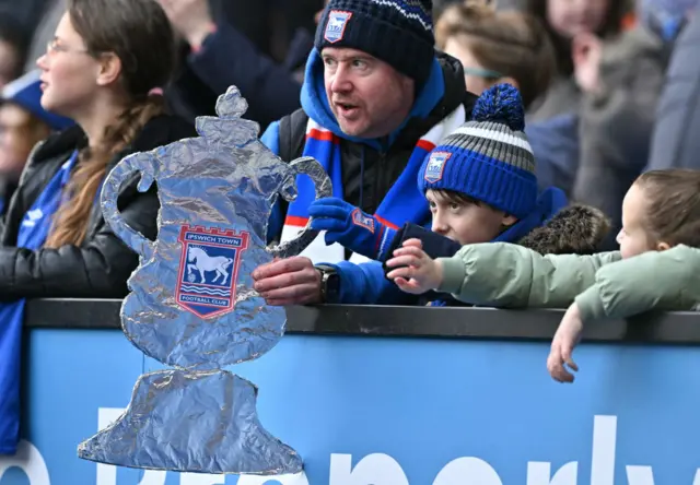 An Ipswich fan sits with his son holding a tinfoil cup.