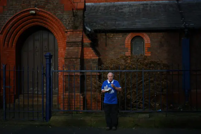 An Everton fan stands and eats chips near Goodison Park.