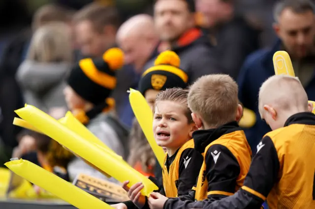 Young Maidstone fans stand with clappers in the stands.