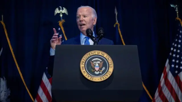 Biden points as he speaks from a lectern decorated with the presidential seal