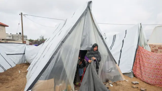 A Gazan woman folds a sheet outside of her makeshift tent home in Rafah