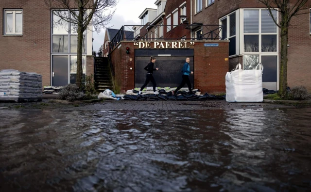 People run past sandbags placed in a flooded street near the Markermeer after the first storm of this year, which was named Henk, in Hoorn, the Netherlands