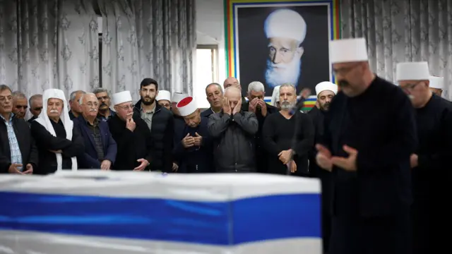 Druze men, in a semi-circle, look on as prayers are said over the casket of killed soldier Sufian Dagash