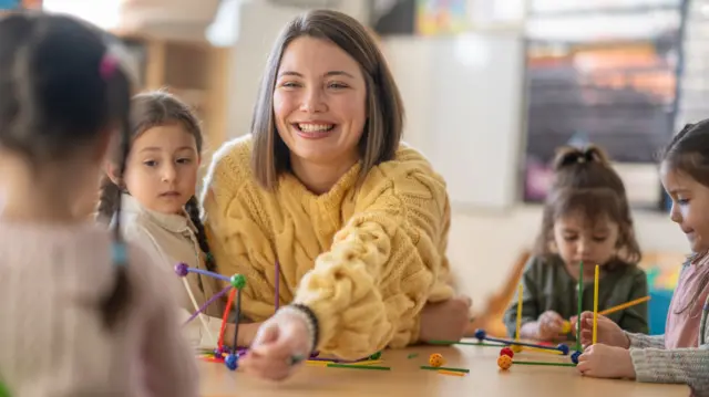 A small group of children sit with their female teacher as they work away building structures.