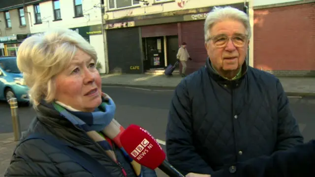 A woman and a man stood next to each other in a street, being interviewed