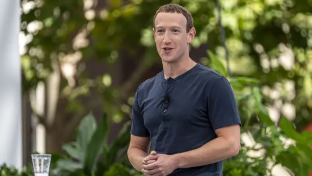 Mark Zuckerberg in a navy t shirt holding his hands