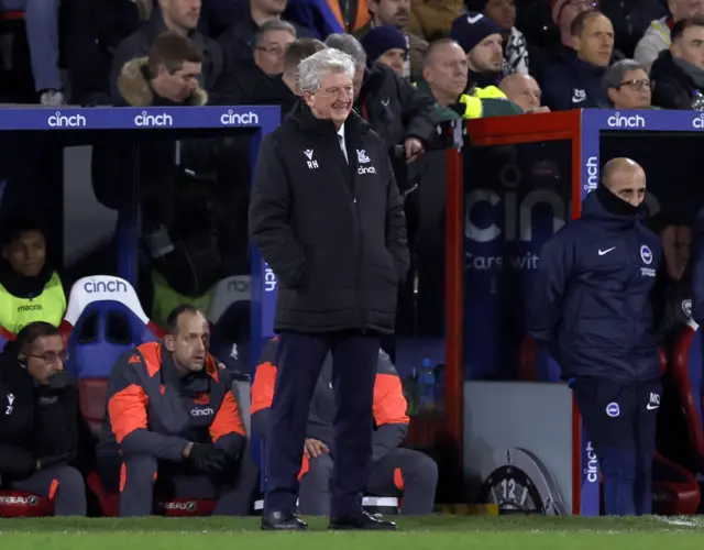 Roy Hodgson stands with his hands in his pockets in front of the dugout.