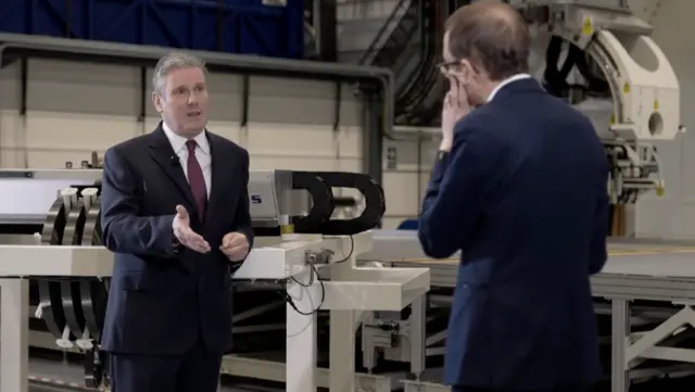 Keir Starmer speaking to Chris Mason with machinery behind them.