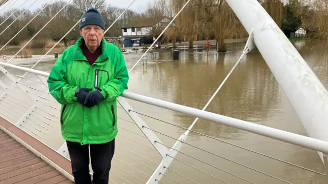 John Lathrope in a green coat standing above the River Great Ouse in Bedford