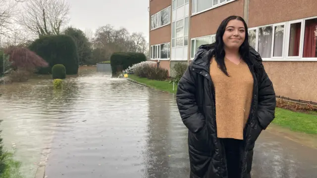 Tia Williamson outside Coton Manor Flats in Shrewsbury, surrounded by flood water.