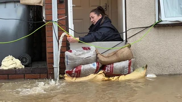 A woman operates a hose to remove water from a house.