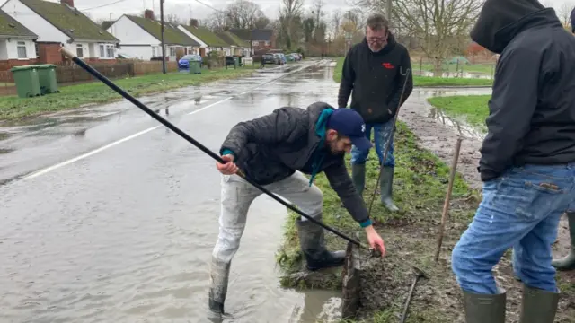 Three men attempt to unblock a drain on a flooded road